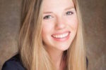 A person with long blonde hair, smiling, in a headshot against a neutral background.