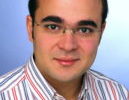 Headshot of a person wearing glasses and a striped shirt, with a neutral expression and a blue background.