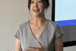 A person in a gray dress is giving a presentation, standing in front of a screen displaying text about an HR specialist.