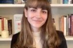 Headshot of a person with long hair and bangs, smiling, in front of a bookcase with various books.